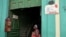 Una mujer parada junto a dos señales de negocios privados en Cuba. 