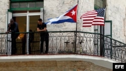 Dos jóvenes cubanos en La Habana conversan junto a las banderas de Estados Unidos y Cuba.